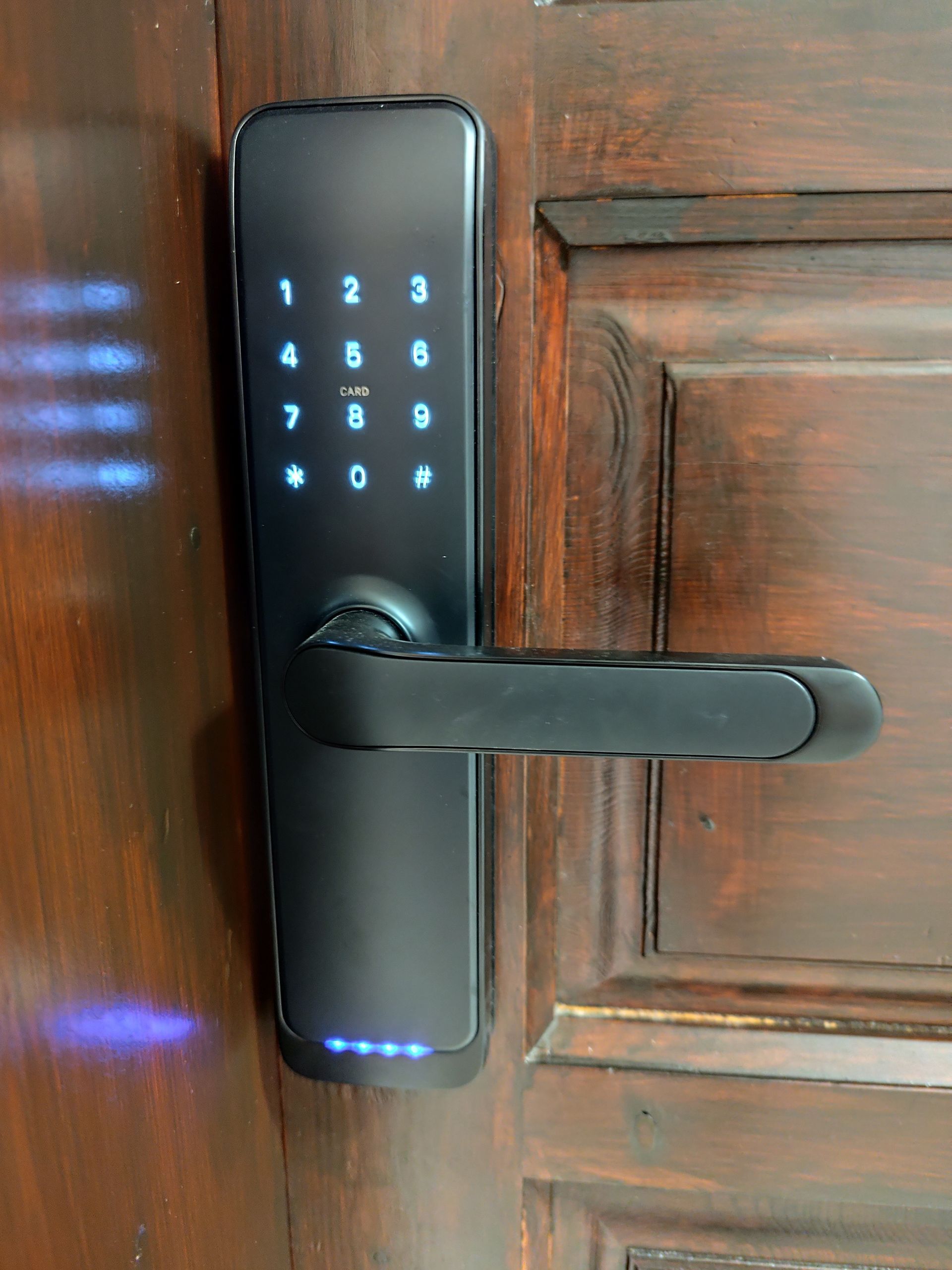 Black keypad door lock on a wooden door, lit with blue indicator lights.