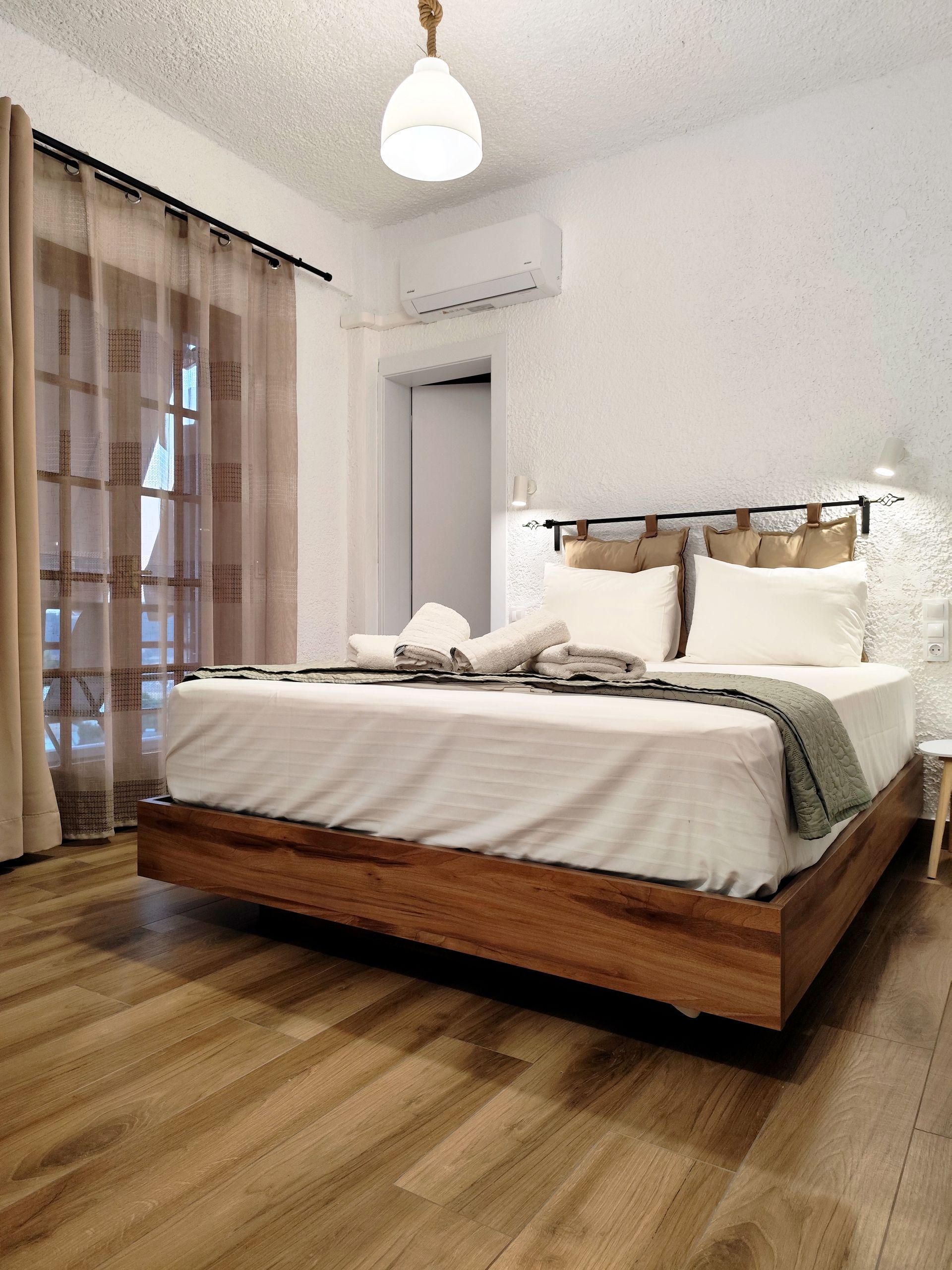 Bright bedroom with a neatly made bed, beige bedding, and sheer curtains by a window.