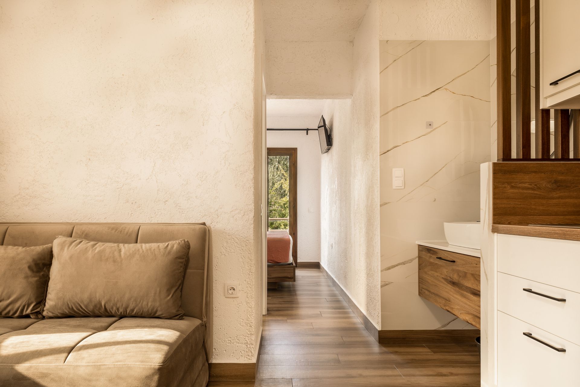 Bright hallway beside a beige sofa, with a white cabinet and wood floor leading to a doorway.