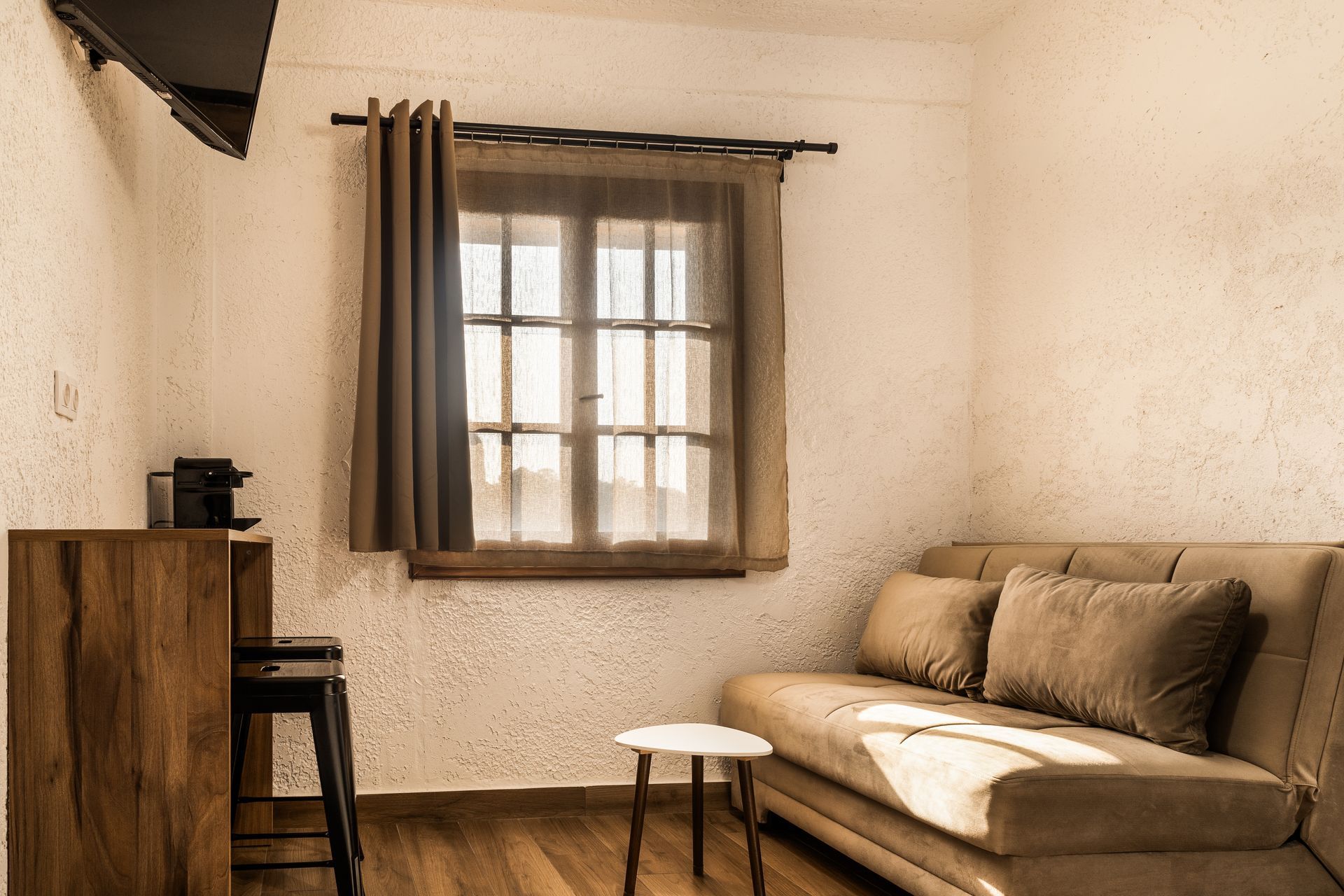 Cozy living room with beige sofa, window, small table, and wooden cabinet in warm light