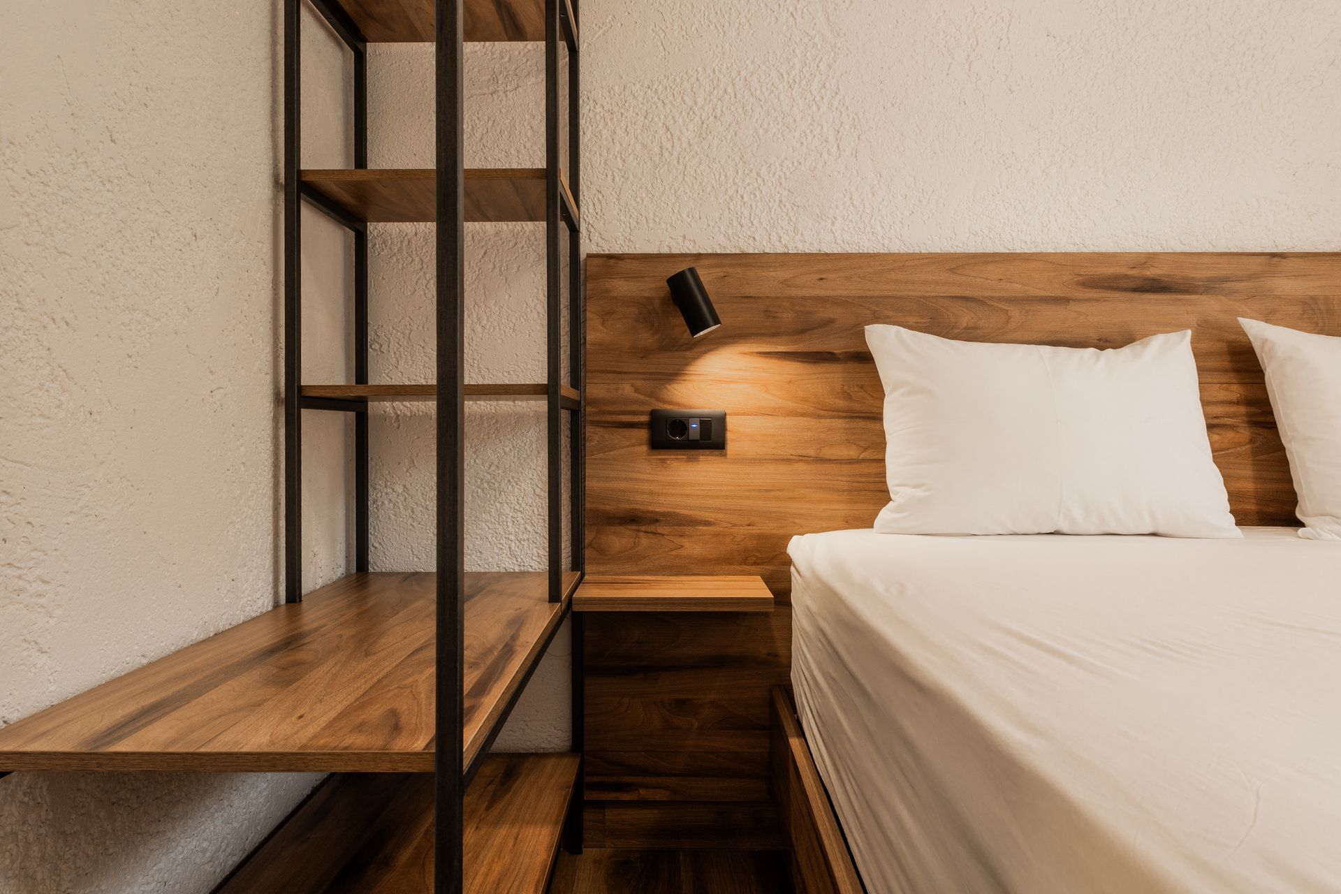 Modern bedroom with wooden headboard, white bedding, and metal shelving unit beside the bed
