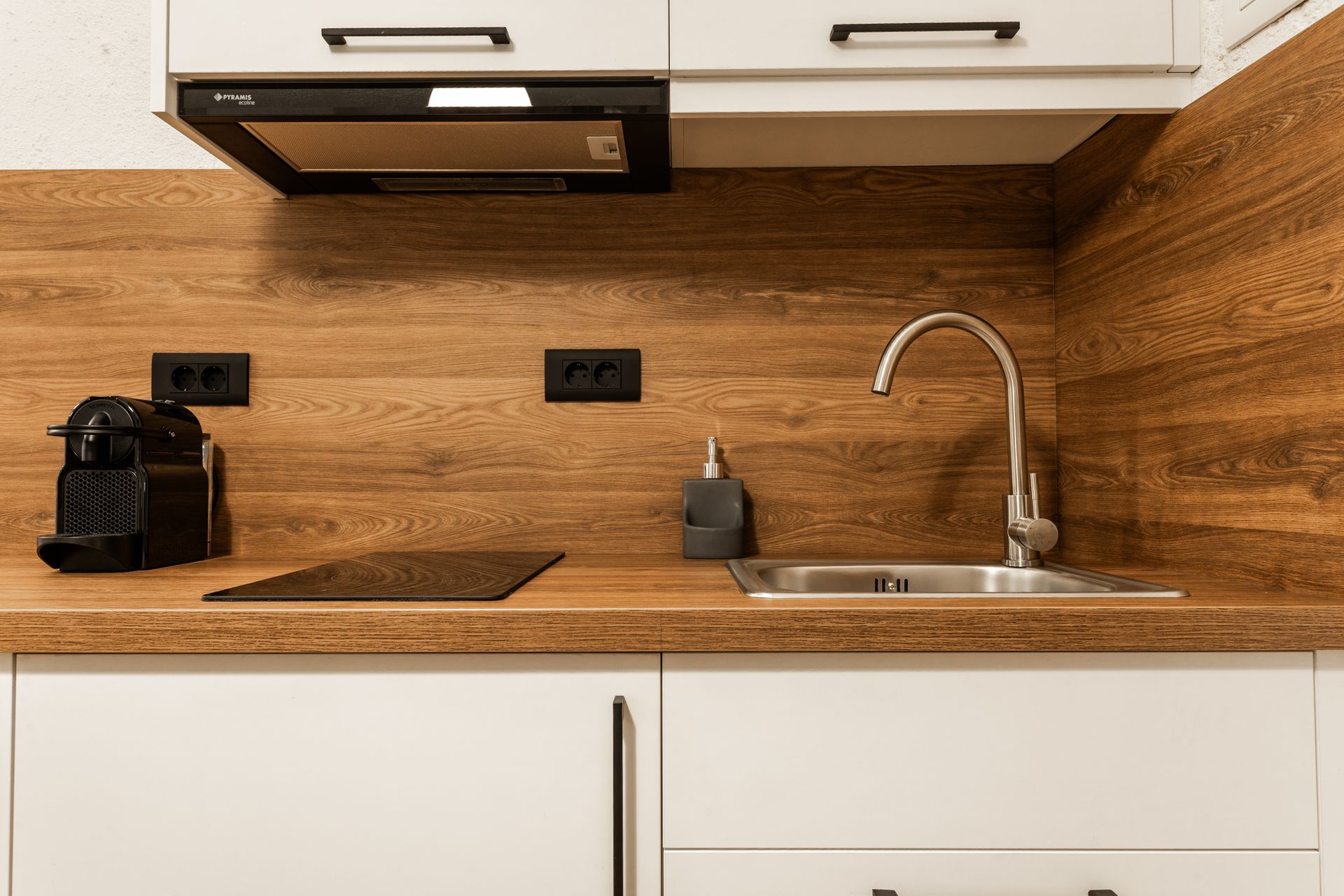 Modern kitchen with white cabinets, wood backsplash, coffee maker, sink, and countertop appliances