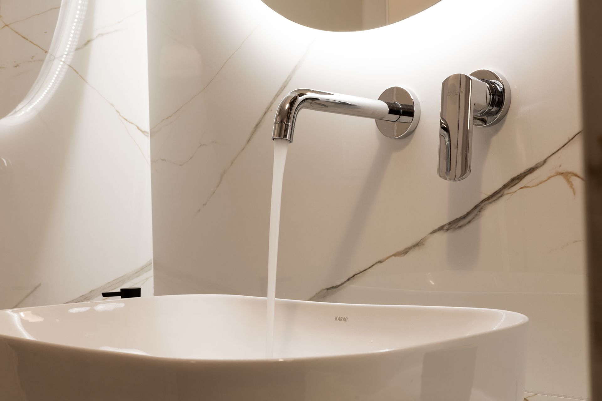 Bathroom sink with running water from a chrome faucet and round mirror above a marble countertop