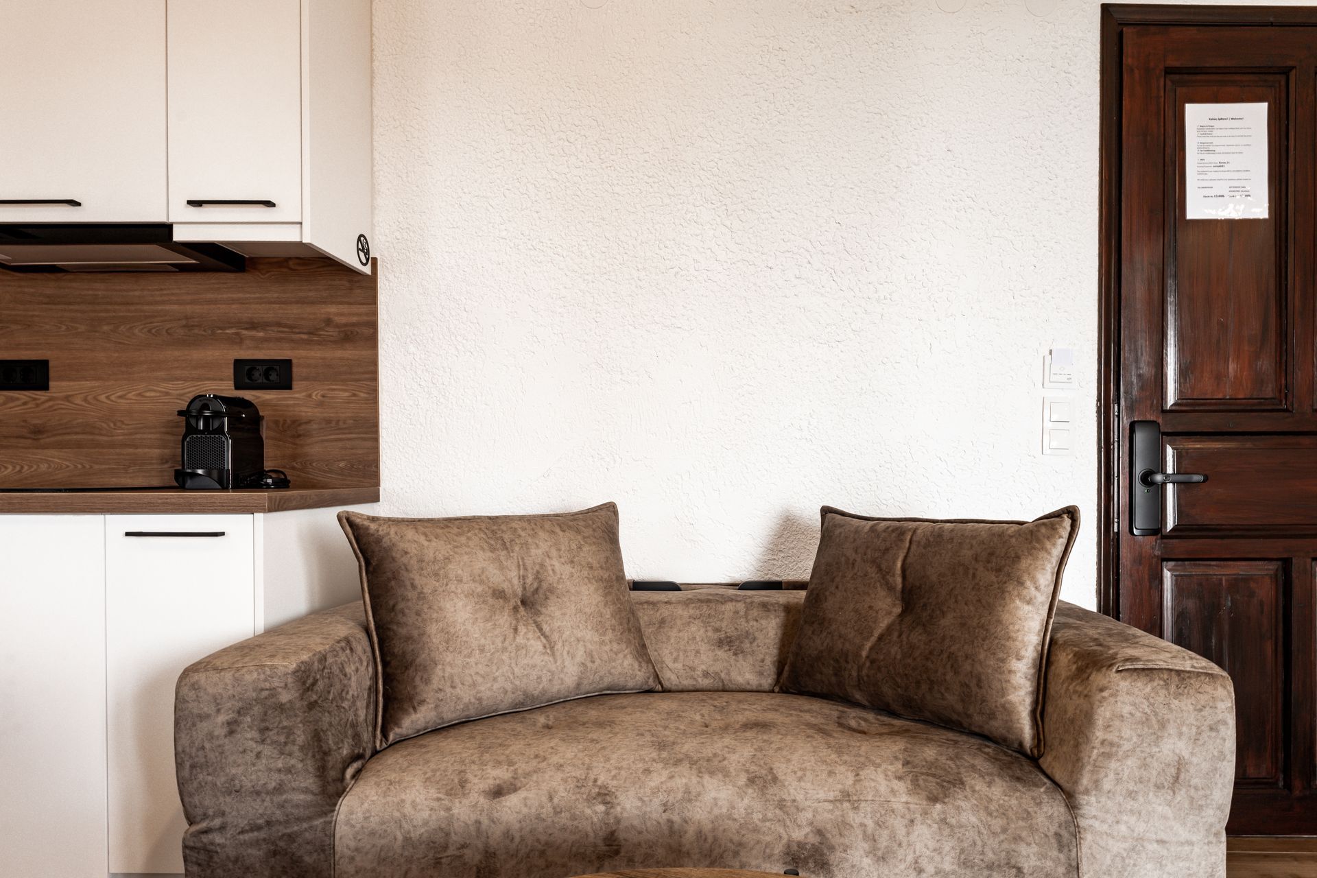 Small living room with a brown sofa, white cabinets, and a wooden door
