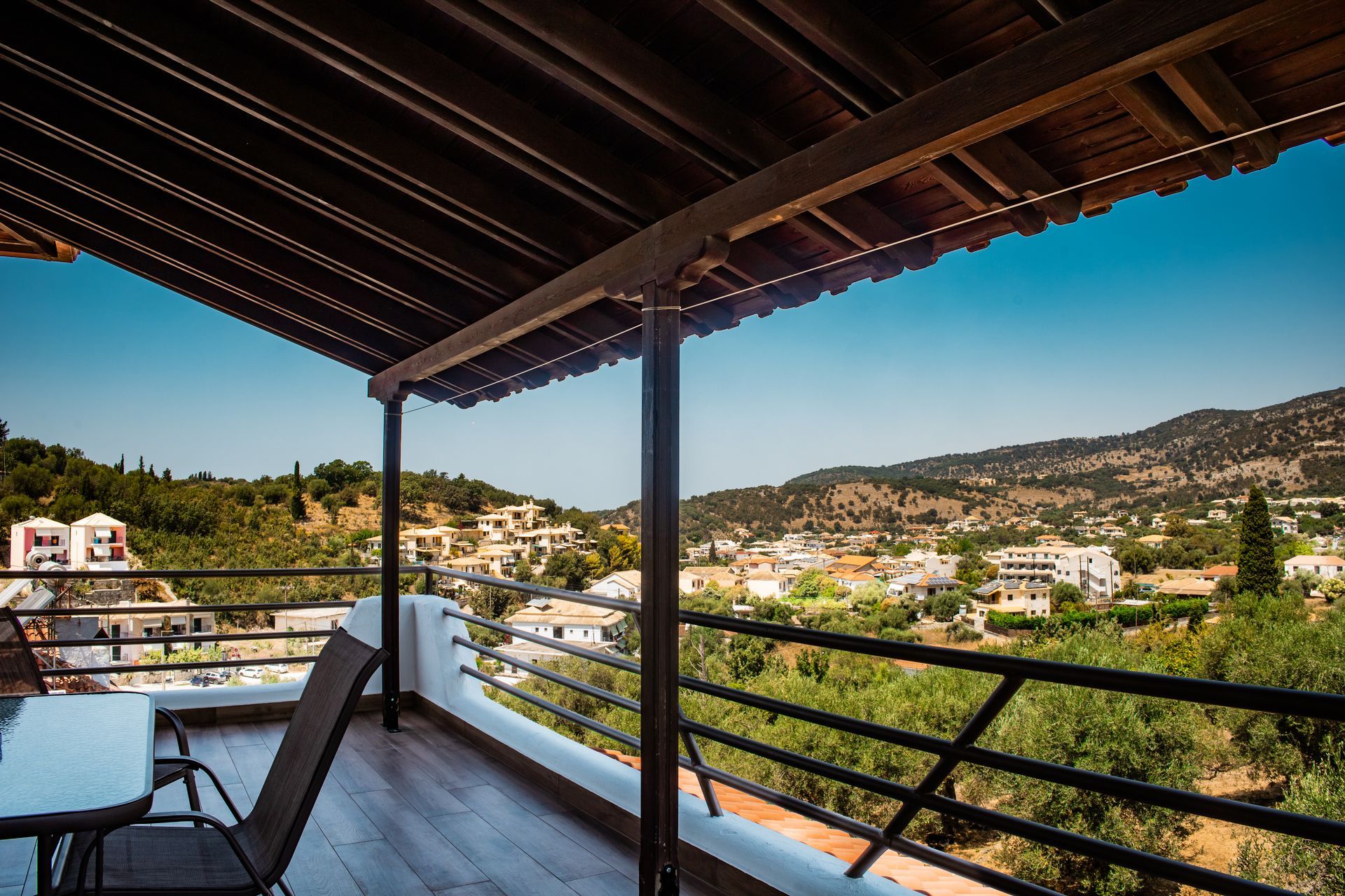 Balcony view over a sunlit hillside town with green trees and blue sky