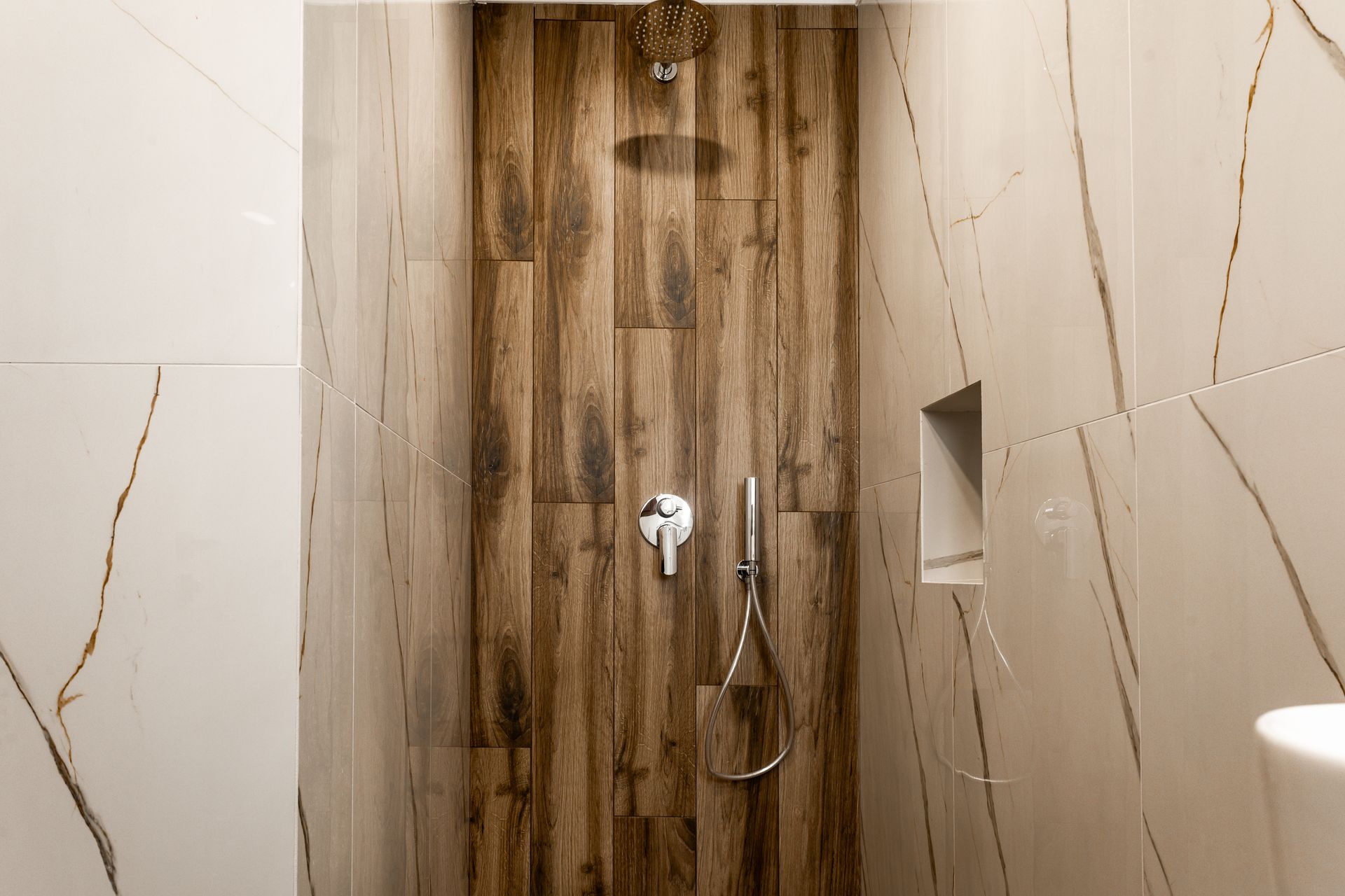Wood-paneled shower stall with beige marble walls and a handheld showerhead.