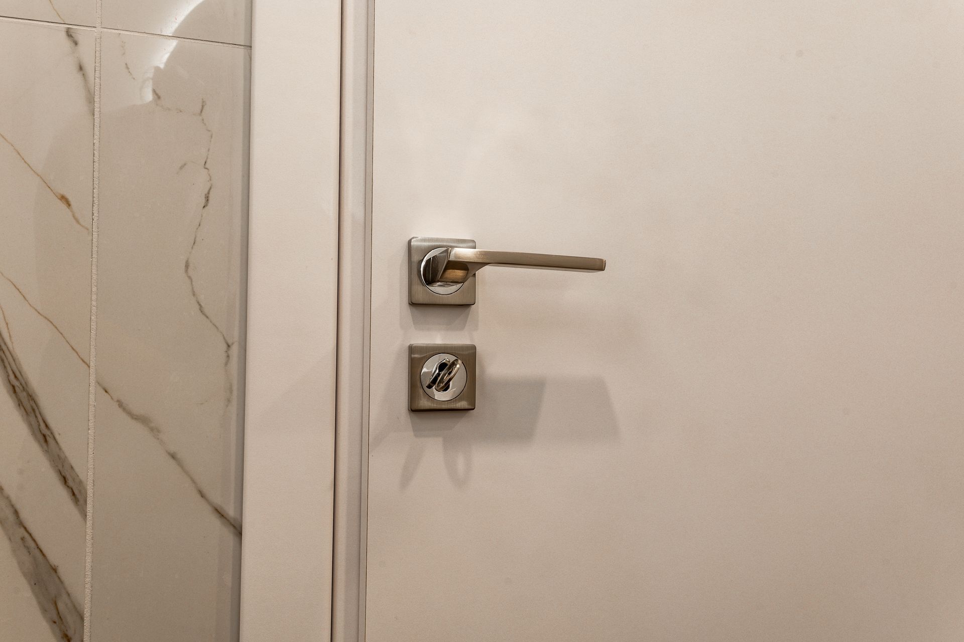 Close-up of a silver door handle and lock on a cream-colored door beside a tiled wall.
