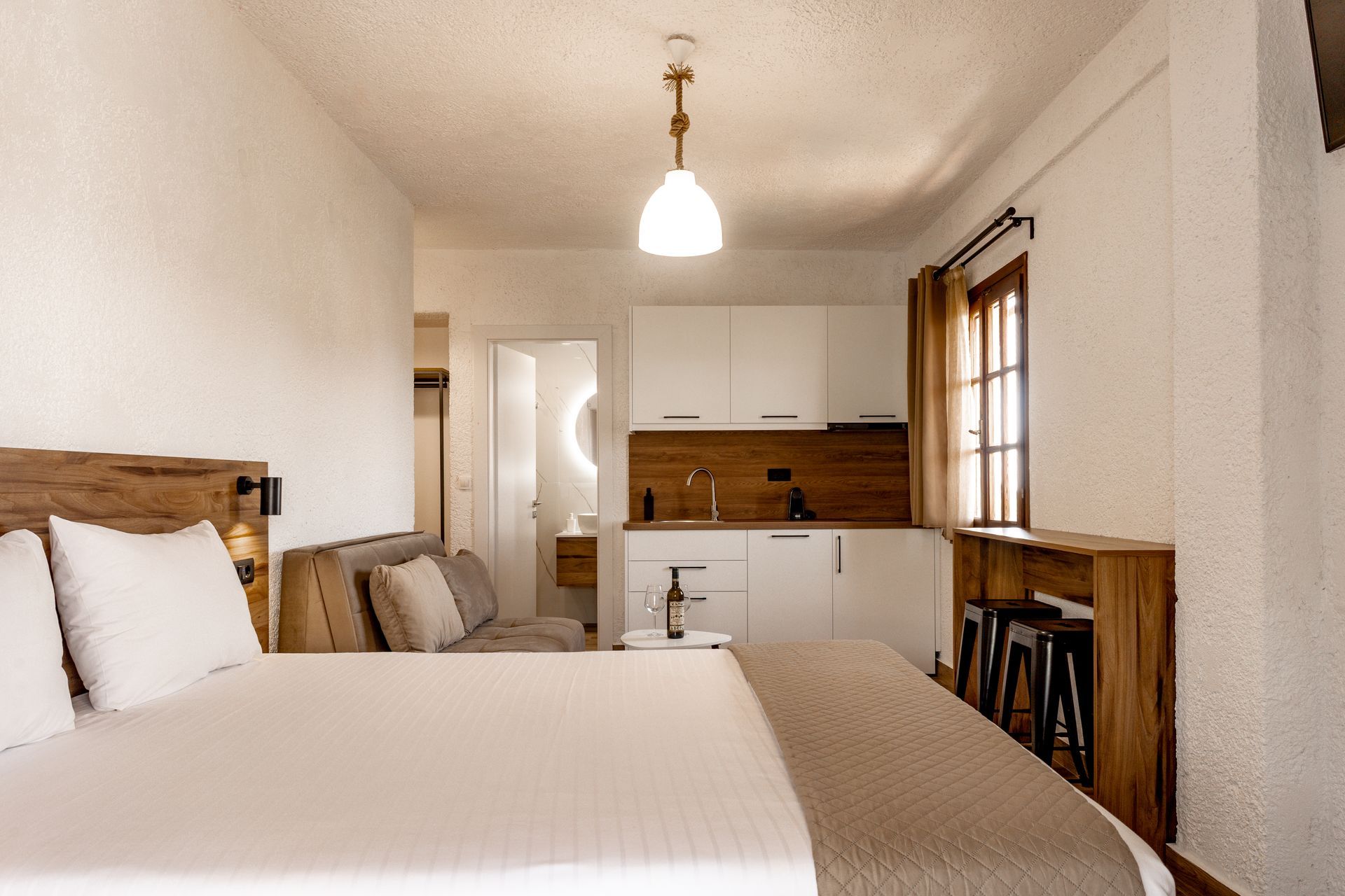 Bright bedroom with a wooden bed, white linens, beige curtains, and a window with a wall-mounted AC unit