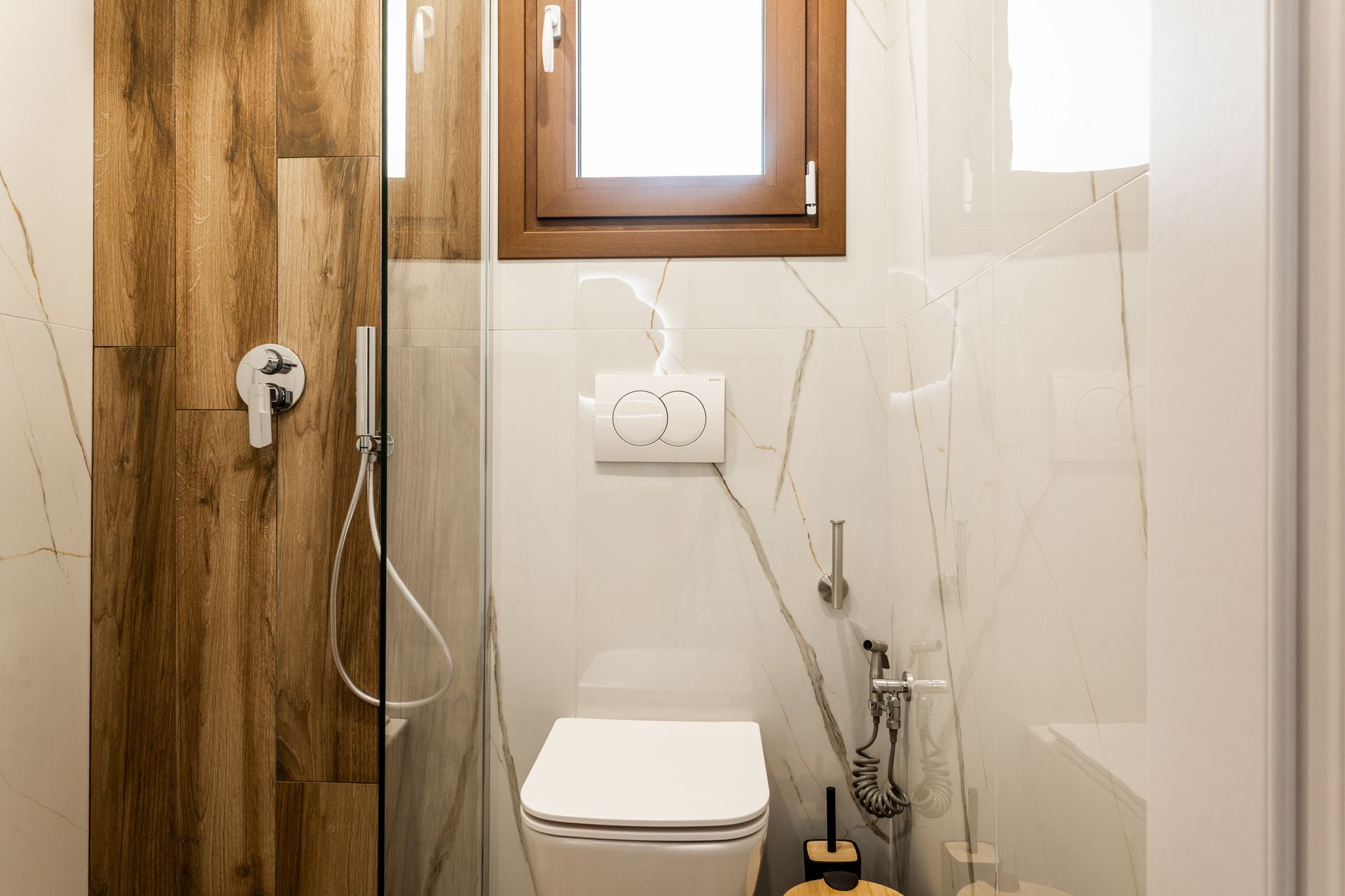 Small bathroom with white toilet, wood-paneled door, and tiled walls under a window.