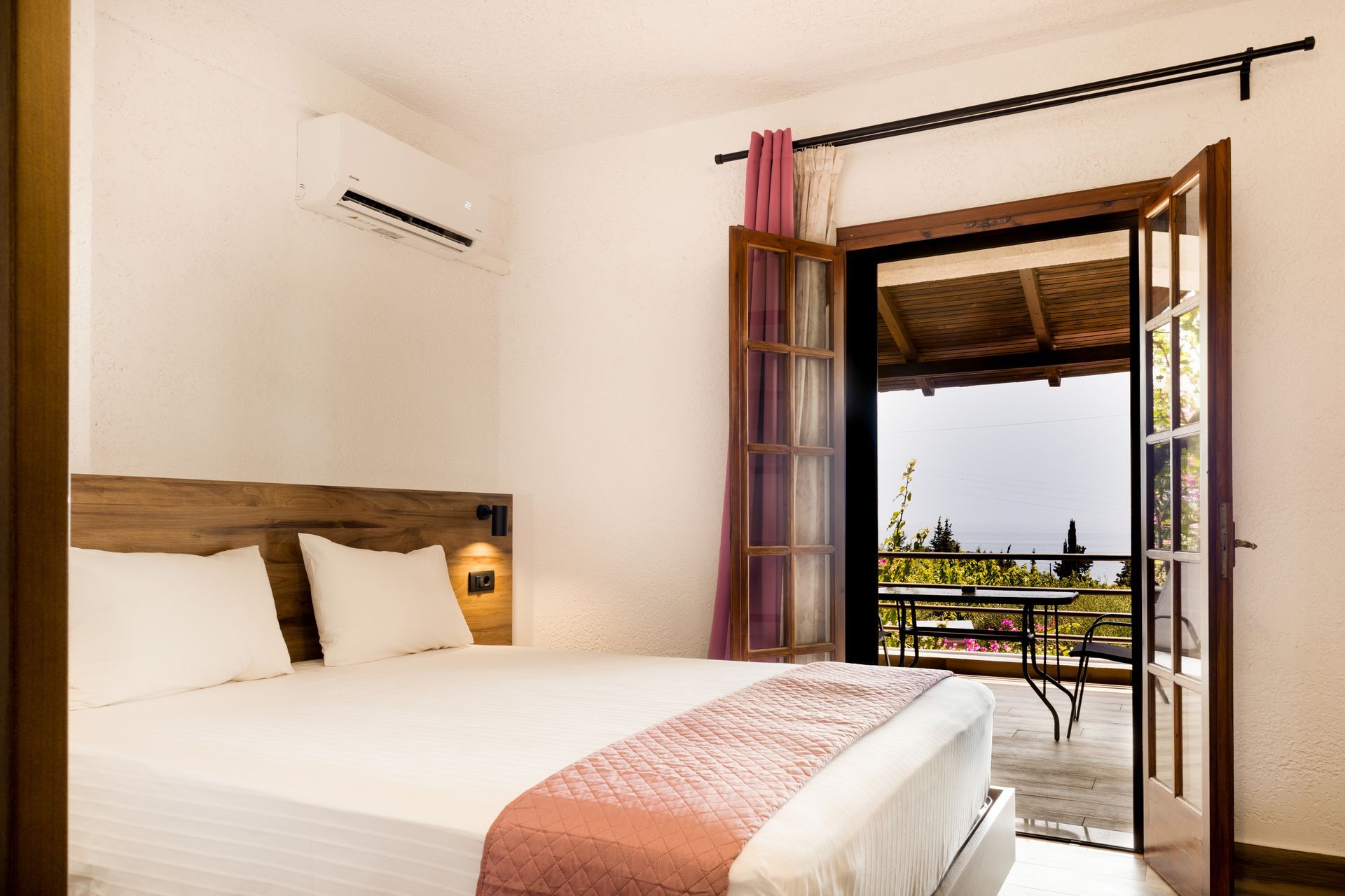 Bright bedroom with a bed, open balcony doors, and a view of the sea