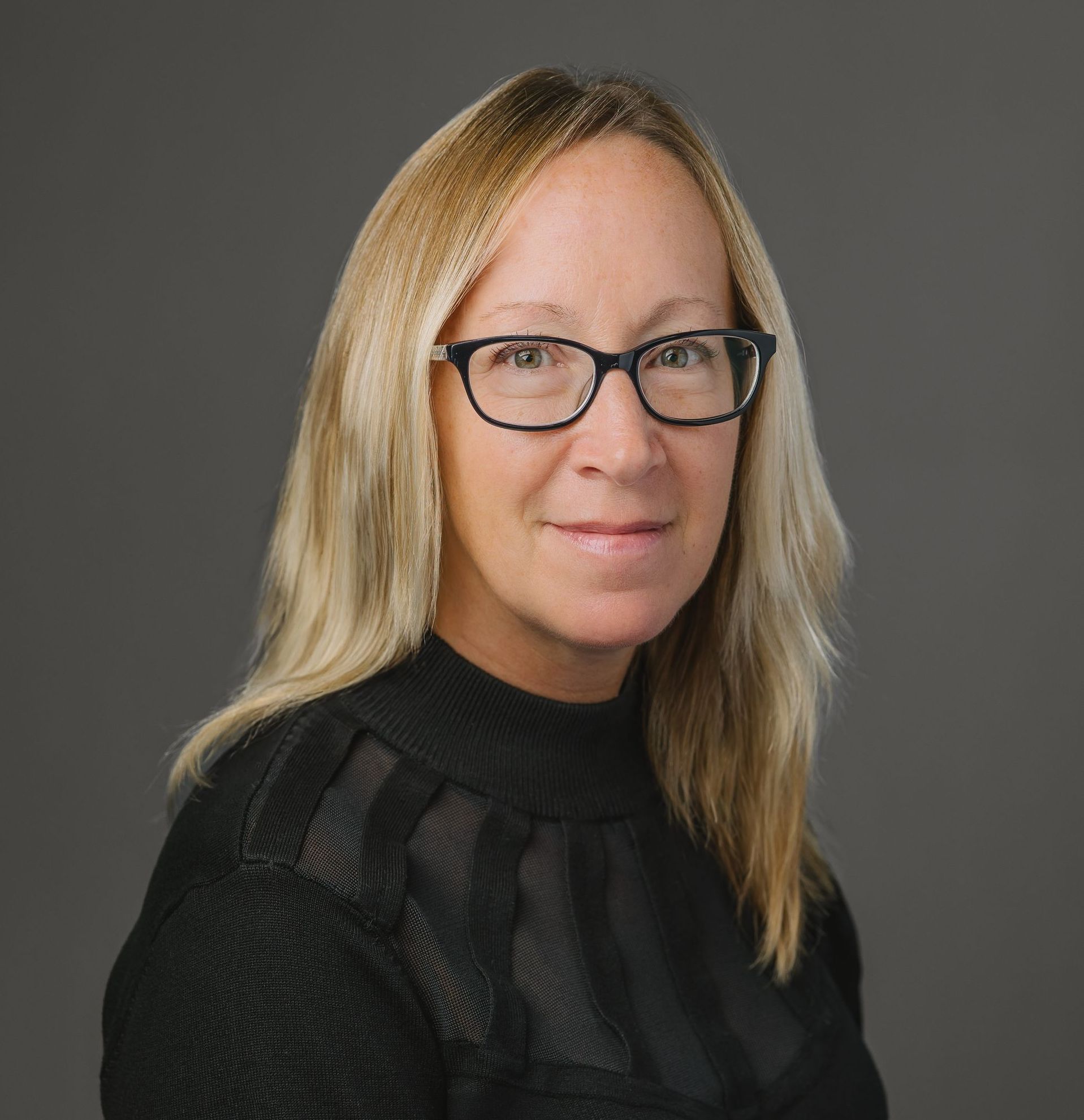 A woman wearing glasses and a black shirt is smiling for the camera.