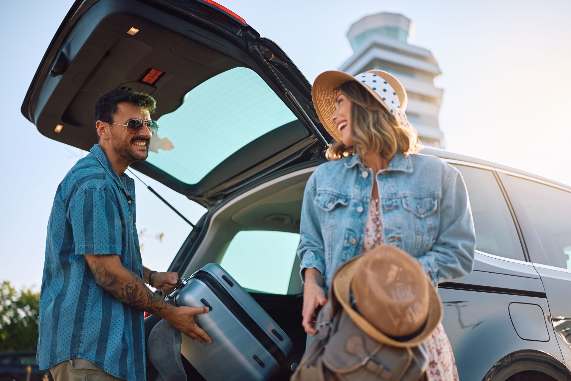 Two people loading luggage into a car with the rear hatch open at sunset