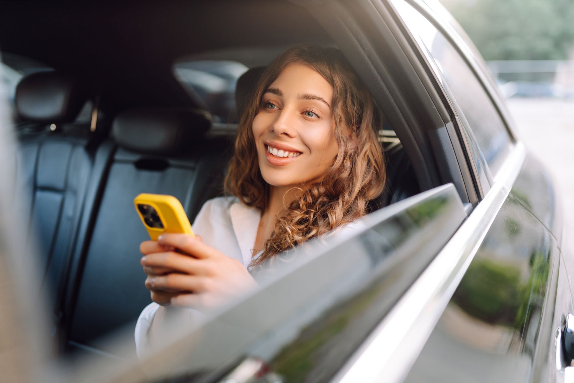 Woman smiling in a car, holding a yellow phone near the window