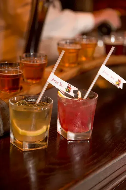 Shot glasses of colorful drinks on a wooden table with straws and cocktail flags
