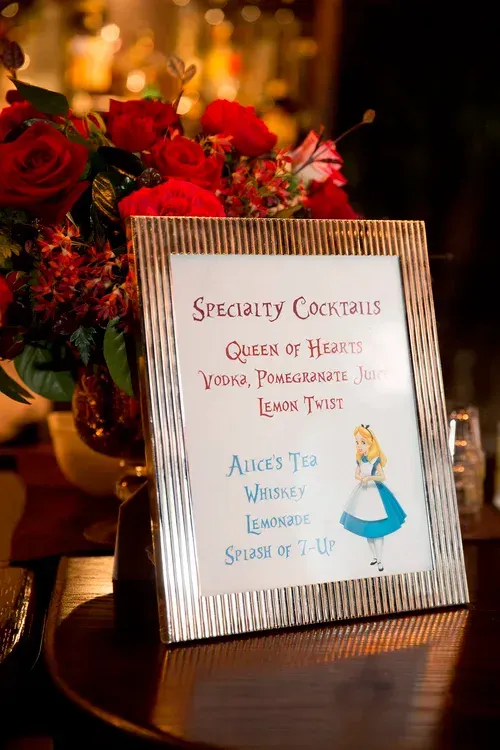 Framed specialty cocktail sign with a red rose design on a warmly lit table indoors