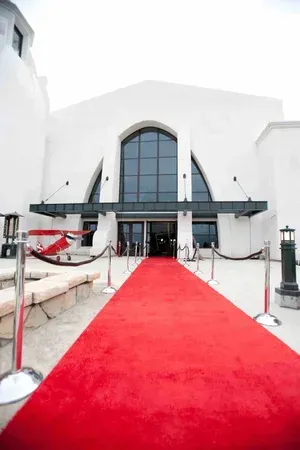 Red carpet leading to a modern white building entrance with a large arched glass door