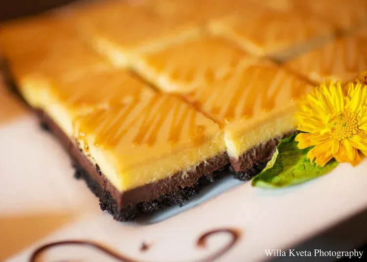 Slice of cheesecake with caramel drizzle and a yellow flower garnish on a white plate