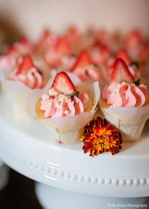 Strawberry dessert cups with pink whipped cream on a white platter with a marigold flower decoration