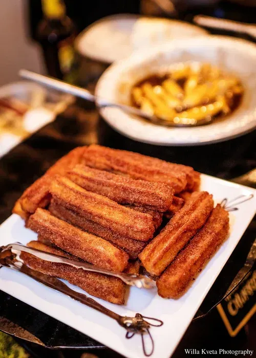 Plate of cinnamon-sugar churros on a table with a blurred bowl of churros in the background