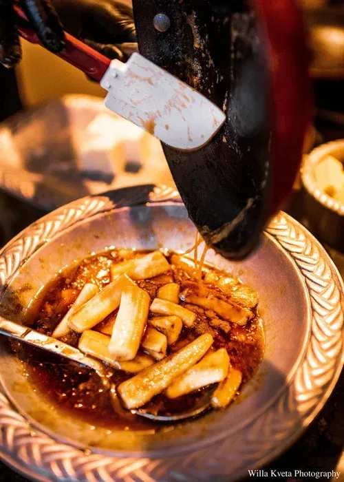 Hot oil pouring into a bowl of fried dumplings or rolls, with sauce and steam in a close-up food shot