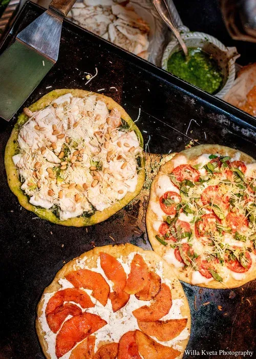 Three pizzas in a dark tray: one white, one red-and-white, and one with pepperoni slices