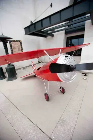 Small red model airplane displayed outdoors on a tiled patio beside a modern building.