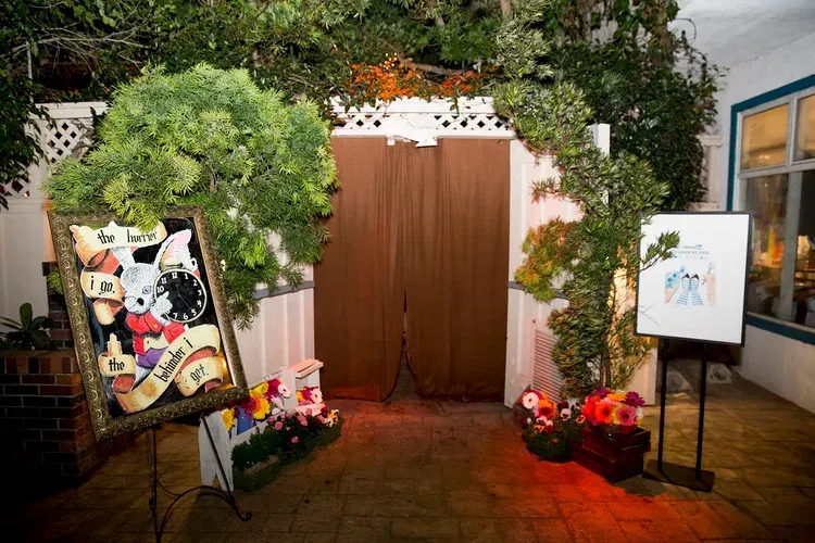 Decorated entrance with flowers, greenery, and art displays flanking brown curtains