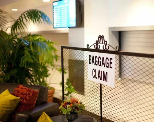 Baggage claim sign in an airport lounge with plants, couch, and a flight information screen.