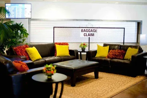Airport lounge seating area with black couches, colorful pillows, and a baggage claim sign in back