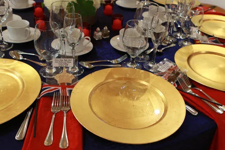 Elegant banquet table with gold plates, red napkins, and glassware on a dark blue tablecloth