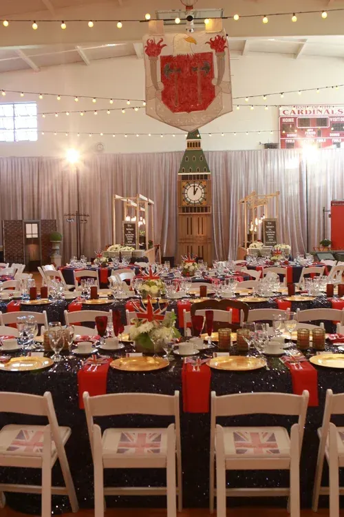 Banquet hall with round tables set for a formal event, red accents, and a large crest banner overhead