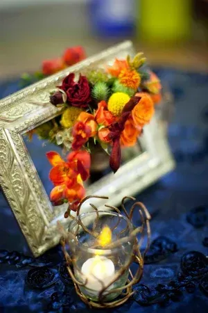 Decorative floral arrangement in a silver frame beside a lit candle on dark blue fabric