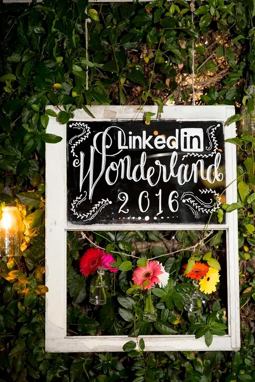 LinkedIn World Café 2016 sign framed by greenery and flowers on a rustic wall