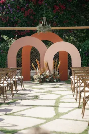 Outdoor wedding aisle with wooden chairs, peach arch decor, and floral arrangement at the altar