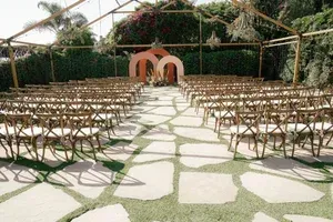 Outdoor wedding ceremony setup with rows of chairs, stone aisle, and peach arch backdrop