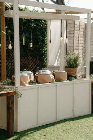 Outdoor white trellis and planter box with hanging lights and potted plants in a garden