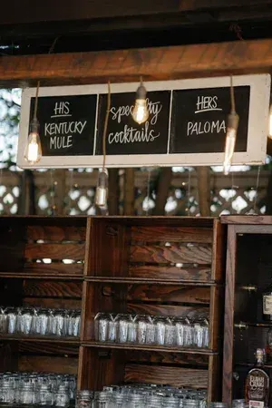 Rustic bar shelf with hanging lights and chalkboard signs for Kentucky Mule, cocktails, and Paloma