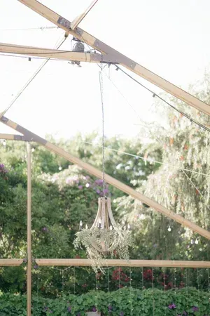 Partially built wooden greenhouse frame with hanging chandelier and plants below