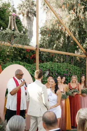 Outdoor wedding ceremony with officiant, couple at the altar, and bridesmaids holding bouquets