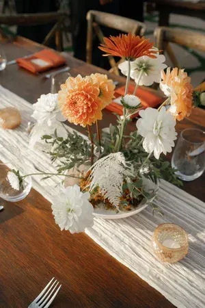 Flower centerpiece with orange and white blooms on a wooden table set for dining