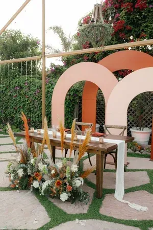Outdoor wedding ceremony setup with wooden chairs, floral arrangements, and large peach arches on a lawn