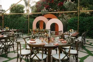 Outdoor dining setup with round tables, white chairs, and a large orange-and-white decorative backdrop