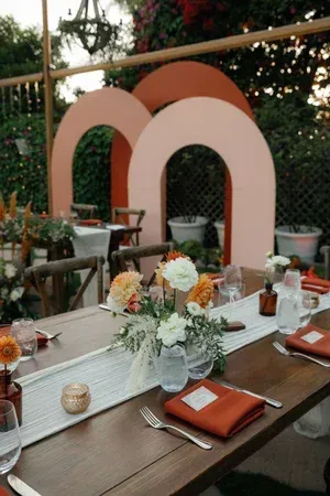 Elegant outdoor dining table with floral centerpiece and coral arch backdrop at sunset