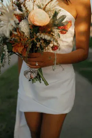 Person in a white dress holding a bouquet of white, peach, and red flowers outdoors