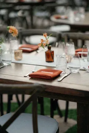 Elegantly set outdoor dining table with orange napkins, glassware, and small flower arrangements
