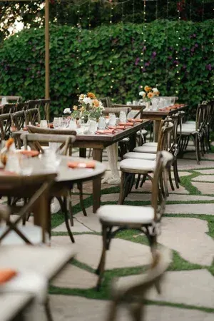 Outdoor café patio with wooden tables, white chairs, and flower arrangements along a vine-covered wall