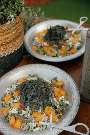 Two bowls of salad with orange fruit and leafy greens on a wooden table