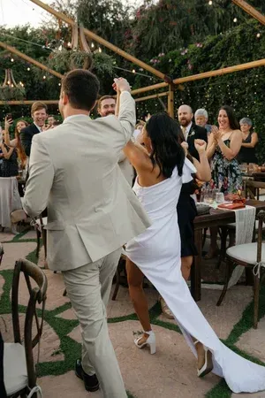 Couple dancing at an outdoor wedding reception under string lights, guests applauding nearby
