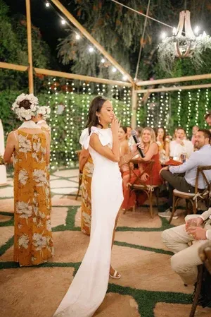 Woman in a white dress speaking at an outdoor wedding reception under string lights