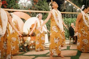 Dancers in golden floral costumes perform outdoors under warm string lights.